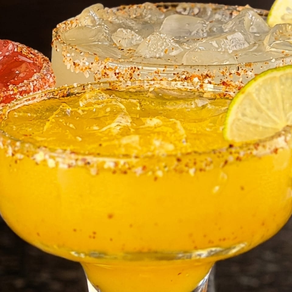 Three vibrant margaritas in red, yellow, and clear, garnished with salt and lime slices.