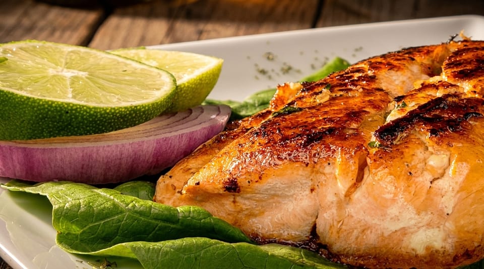 Grilled salmon fillet on a bed of spinach, garnished with lime wedges and red onion slices.