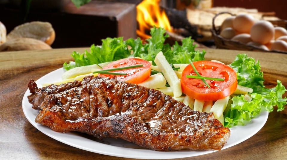 Grilled steak with french fries, lettuce, and tomato slices on a white plate, with a fireplace in the background.